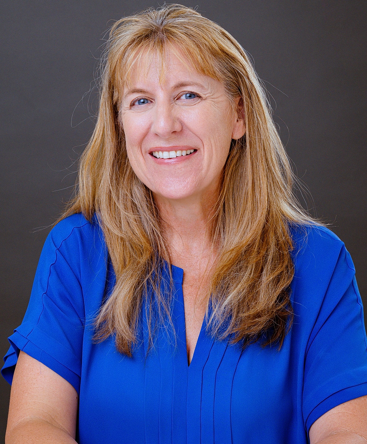 Smiling woman with long hair in blue shirt.