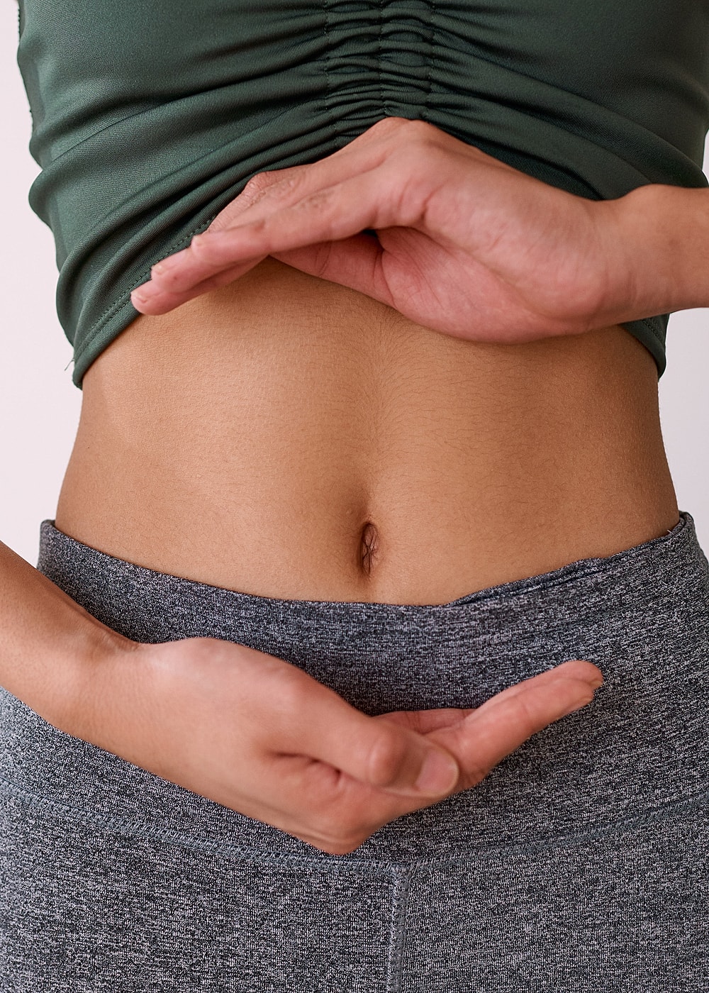 Showing hands around a woman's abdomen region.