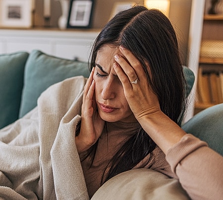 Woman with headache sitting on couch.