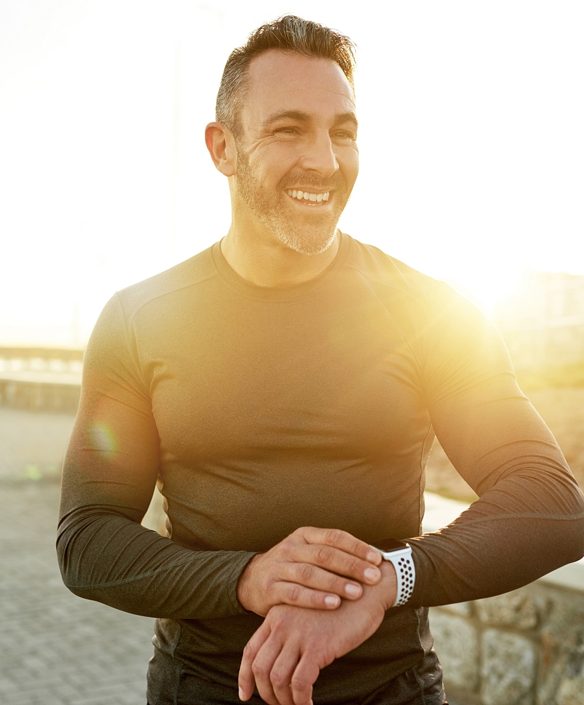 Smiling man checking watch in sunny background