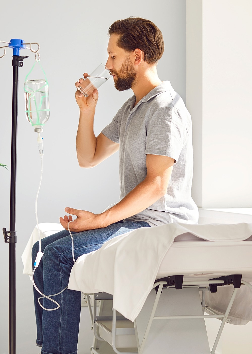 Man sitting, drinking water next to IV drip.