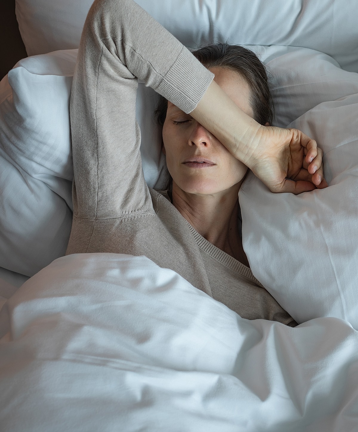 Woman resting in bed, arm over face.