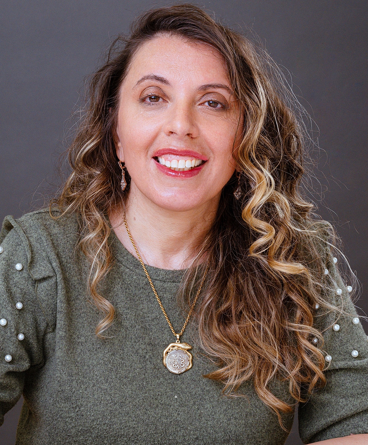 Smiling woman with curly hair and necklace.