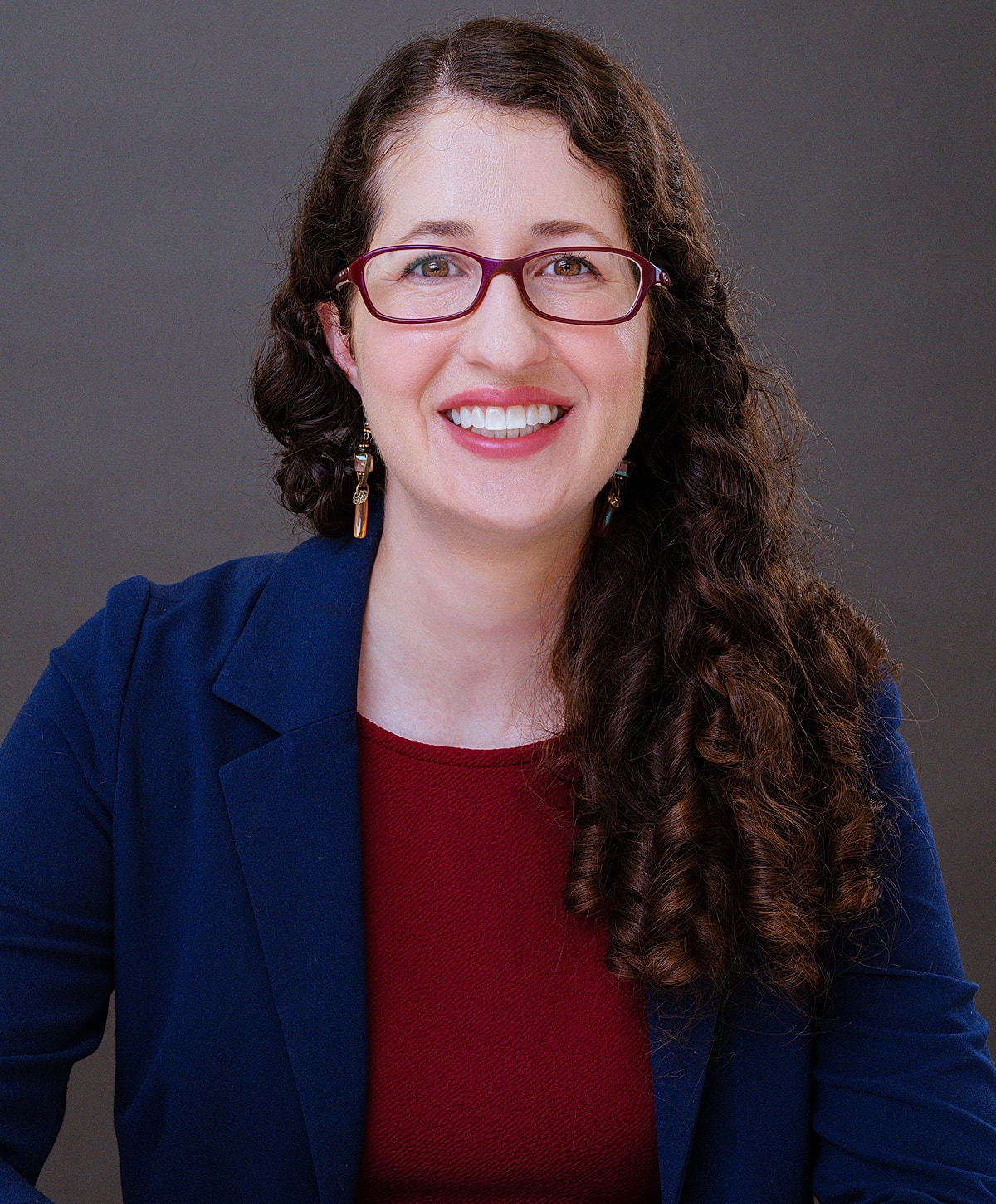 Woman smiling, wearing glasses and a blazer.
