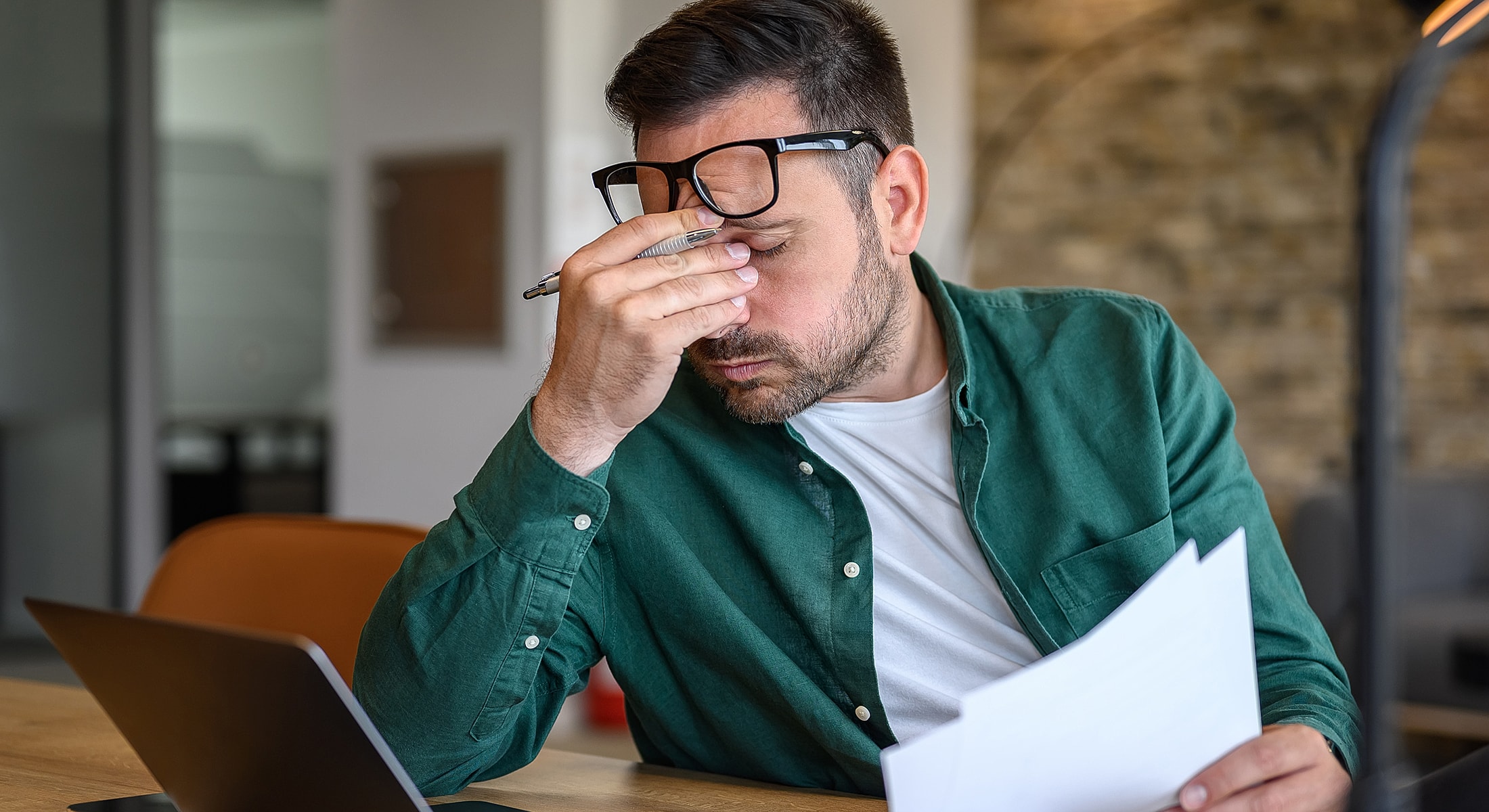 Man stressed at work with documents and laptop.